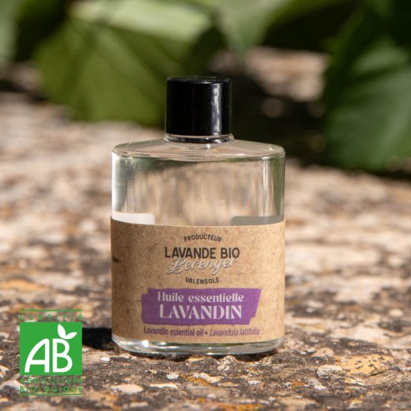 A glass bottle of Lavender essential oils 10 to 50 ml dropper sits outdoors on a stone surface, labeled "Huile essentielle LAVANDIN" with the AB (Agriculture Biologique) organic certification logo in the bottom left.